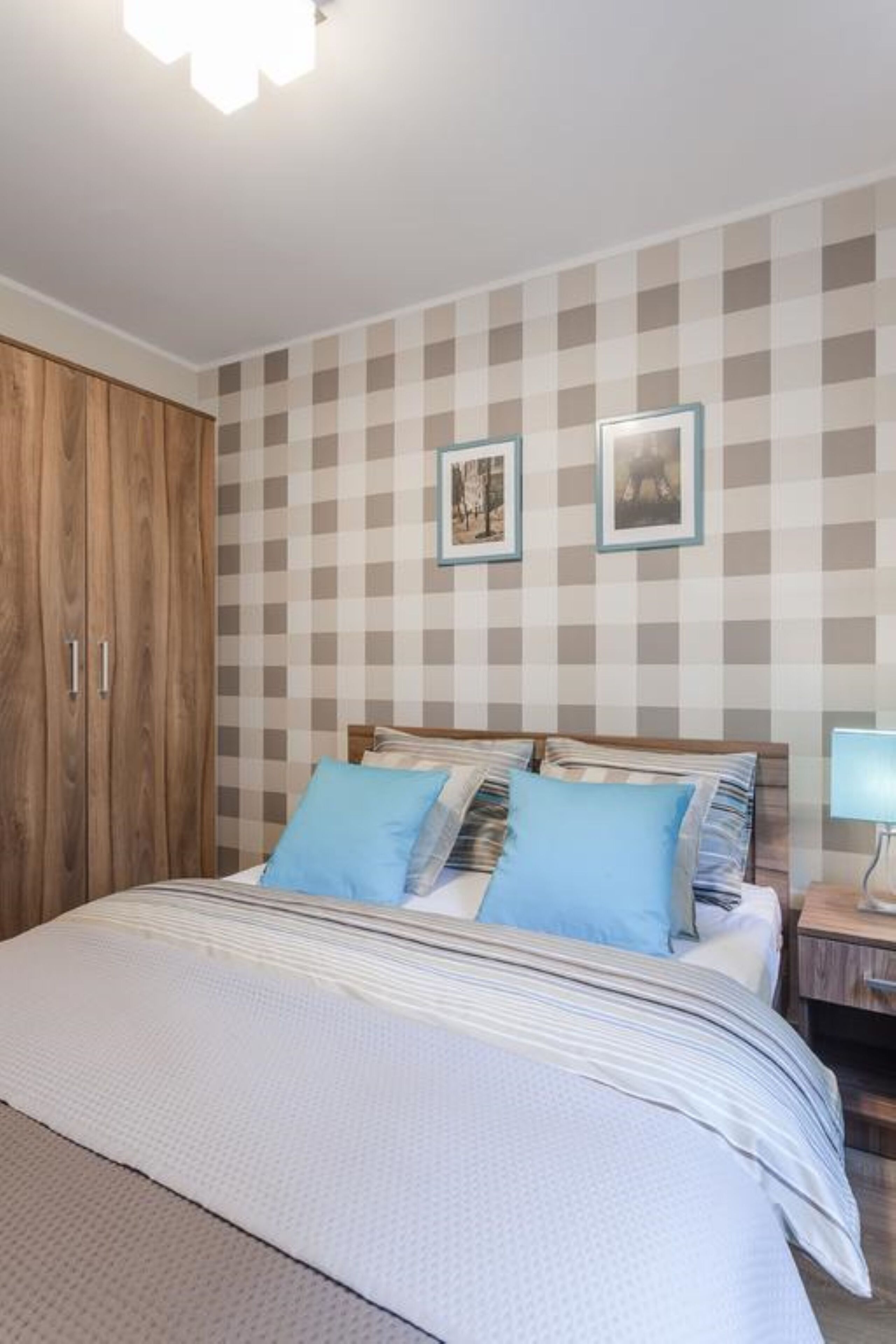 Une chambre avec un mur à carreaux, un lit avec des coussins bleus, une armoire en bois et une table de chevet avec une lampe.