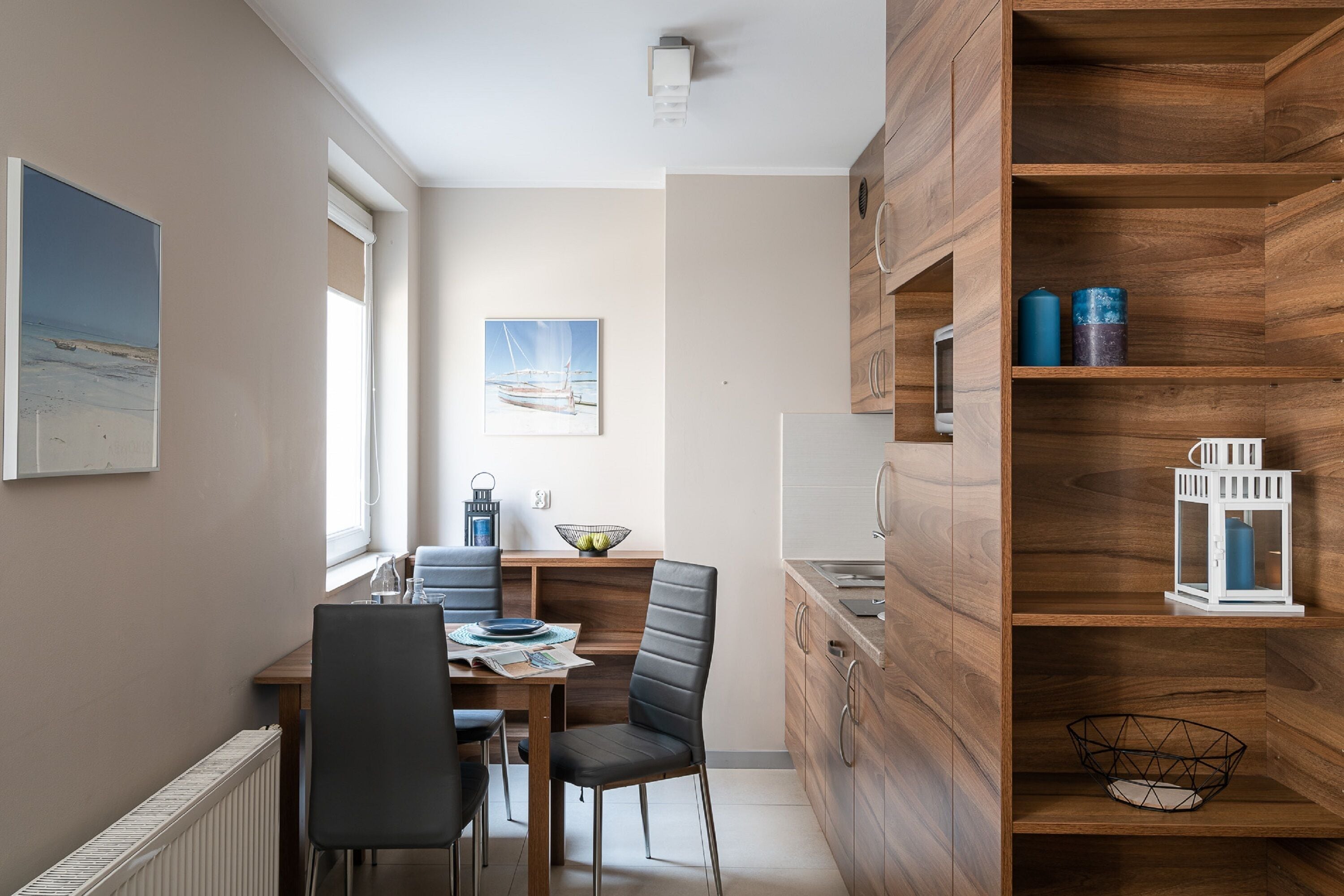 Eine kleine Küche mit Holzausstattung, ein Essbereich mit Tisch und Stühlen sowie ein Fenster für natürliches Licht.