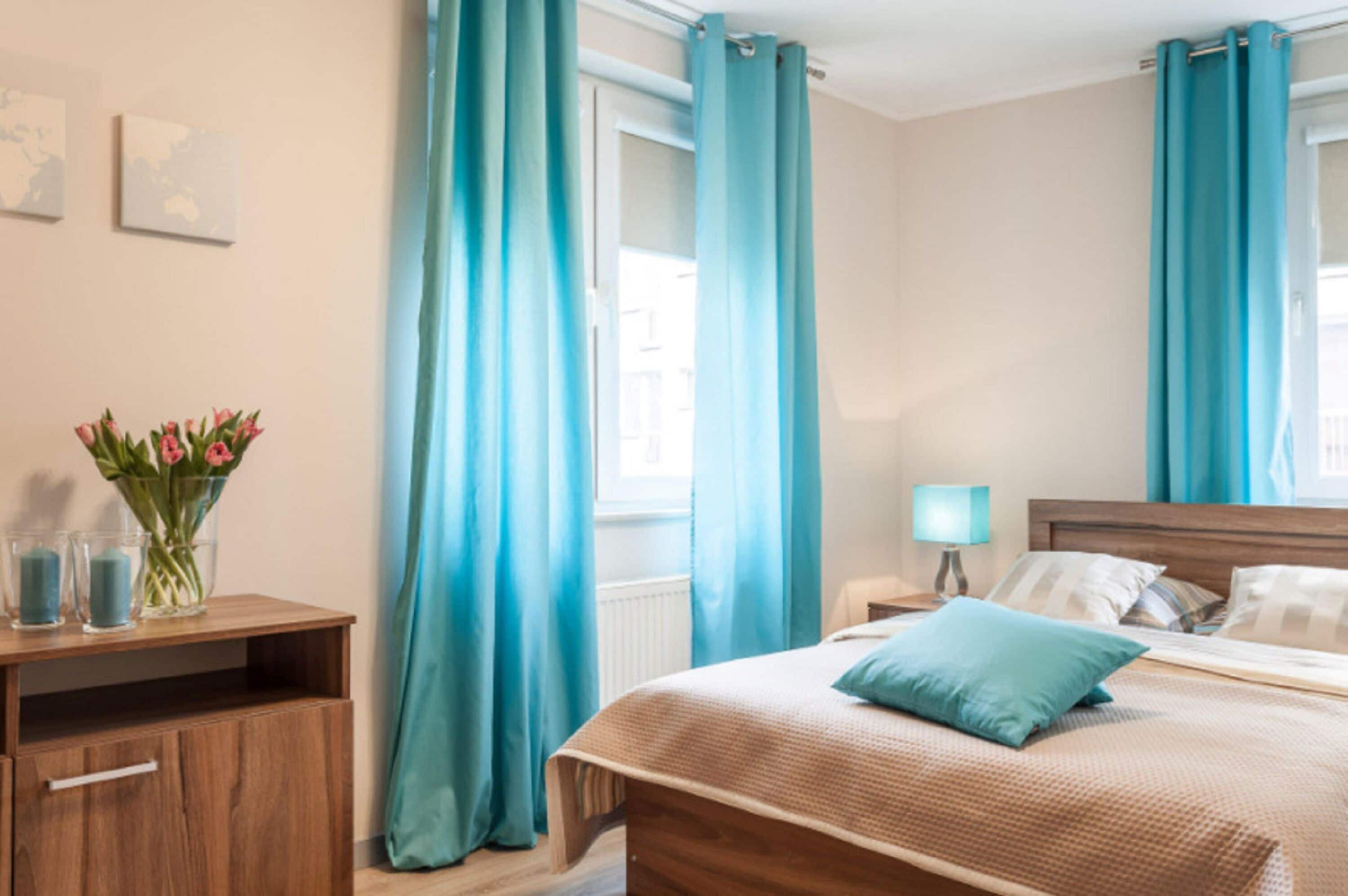 A hotel room with a wooden bed, a nightstand with a lamp, and a window with curtains.