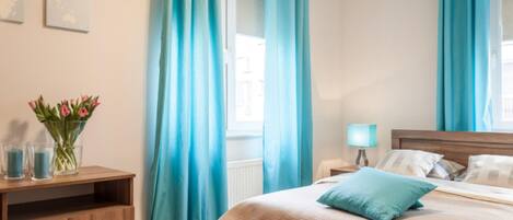 A hotel room with a wooden bed, a nightstand with a lamp, and a window with curtains.