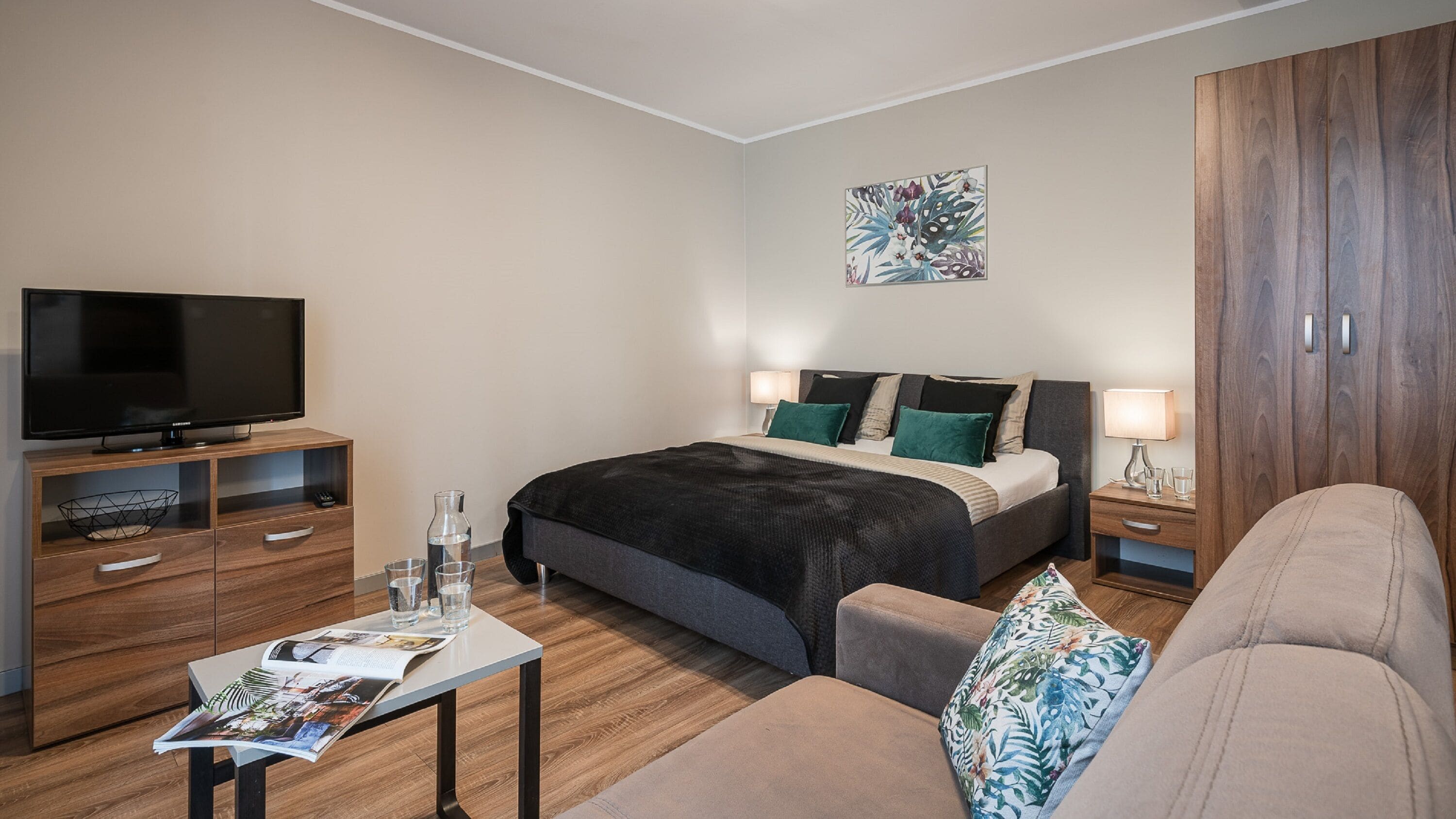 Habitació d'hotel moderna amb un llit, una televisió, una taula petita amb una revista i un sofà.