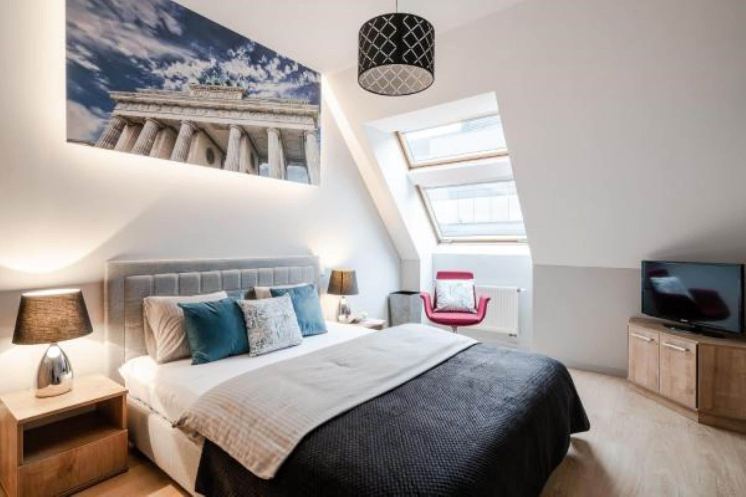 Ein Schlafzimmer mit Bett, Nachttischen, einem Fernseher, einem Sessel und einem großen Fenster.