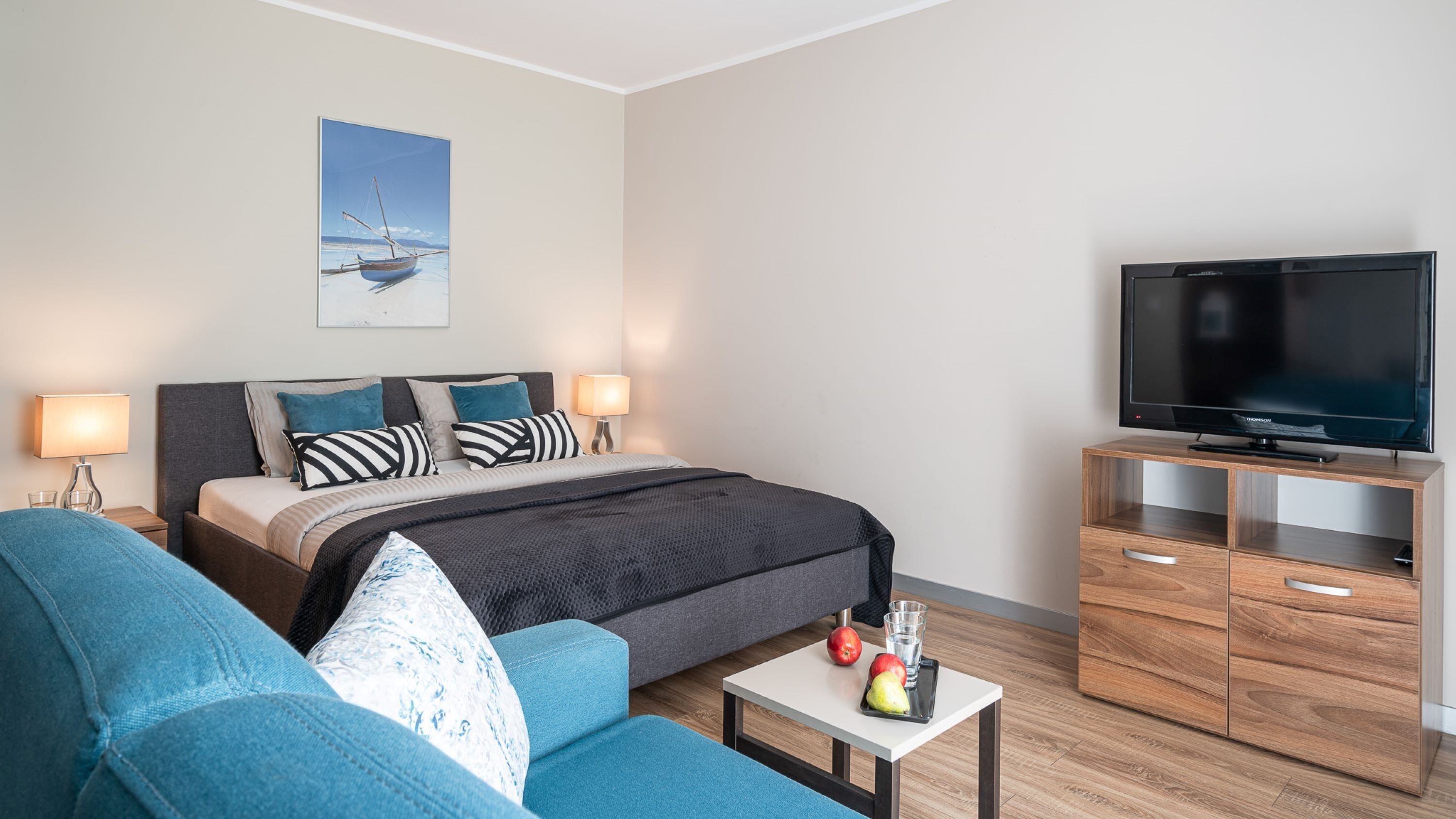 A modern hotel room with a bed, a TV, a sofa, and a coffee table.