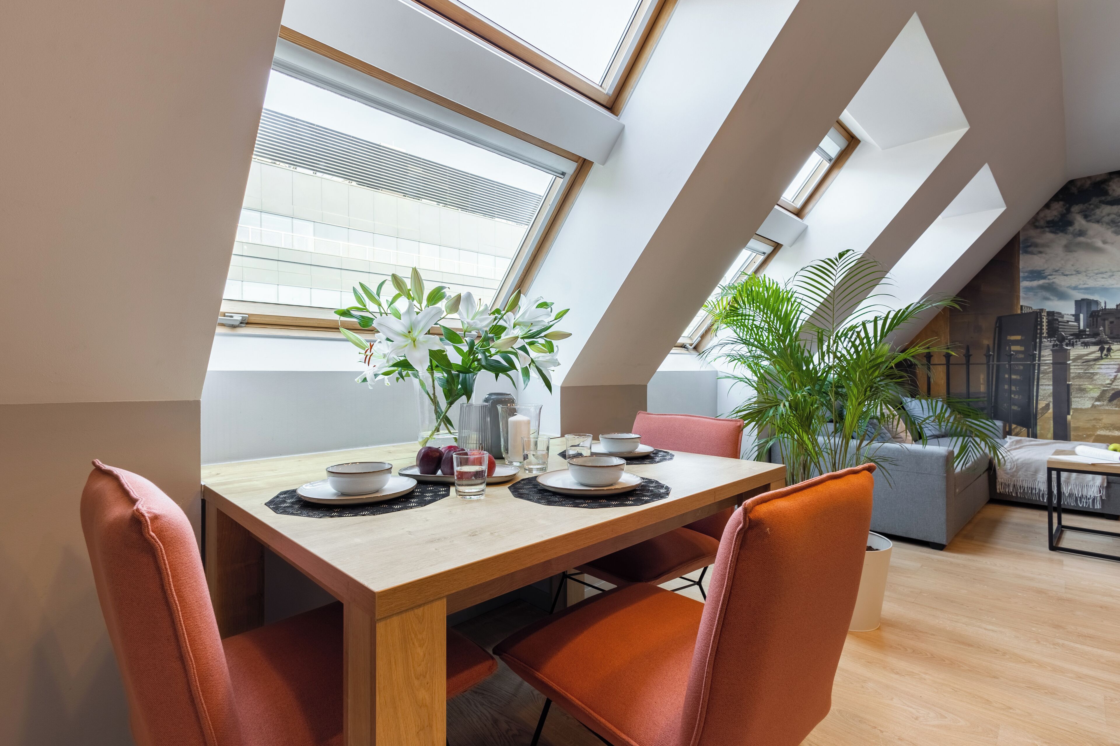 A dining area with a wooden table, orange chairs, and a cityscape mural on the wall.