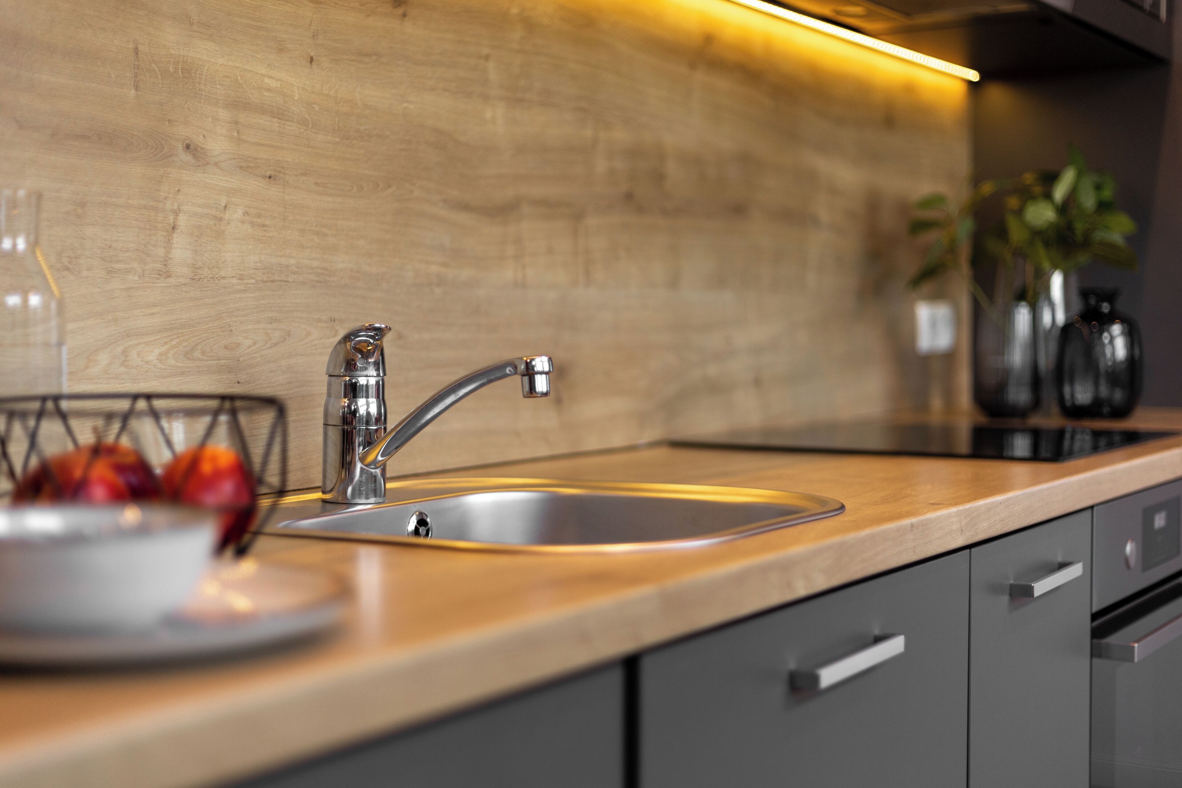 Eine moderne Küche mit Spüle aus Edelstahl, einer Holz Arbeitsplatte und grauen Schränken.