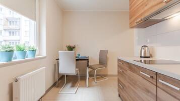 A compact kitchen with a dining area, a radiator, wooden cabinets, and a window with potted plants.