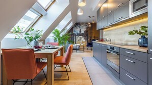 A modern kitchen with skylights, a dining area with a wooden table and orange chairs, and a view of a cityscape through a large window. - Absynt Apart Wierzbowa (Wroclaw)