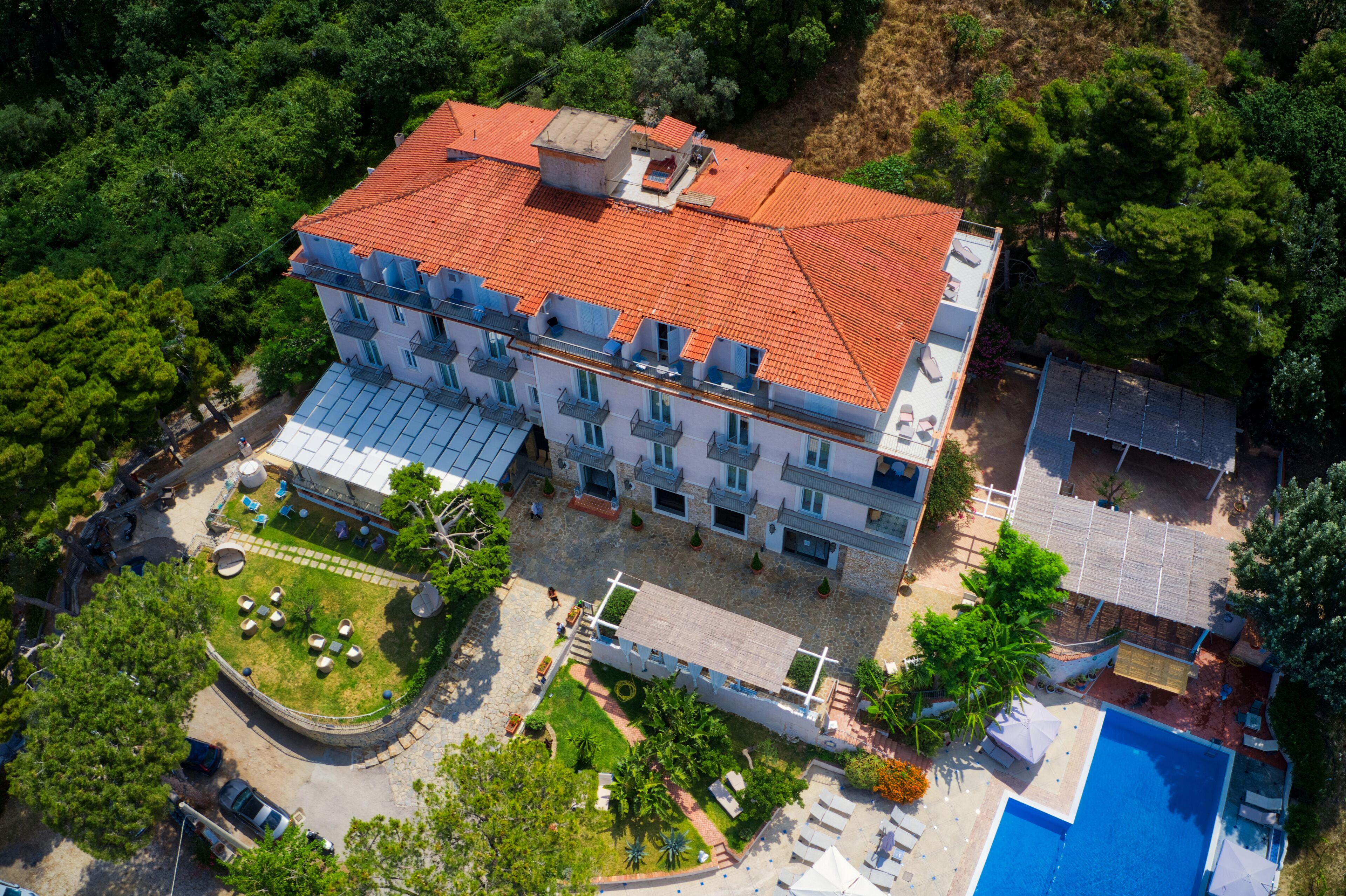 Vista aérea de un hotel con varios pisos, techo de tejas rojas y una piscina.