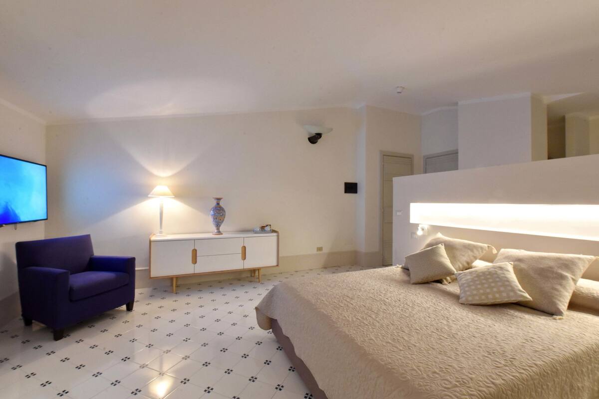 A bedroom with a bed, a chair, a nightstand, and a TV.