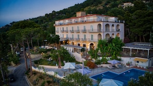 A multi-story hotel with a pool, outdoor seating, and a lush garden.
