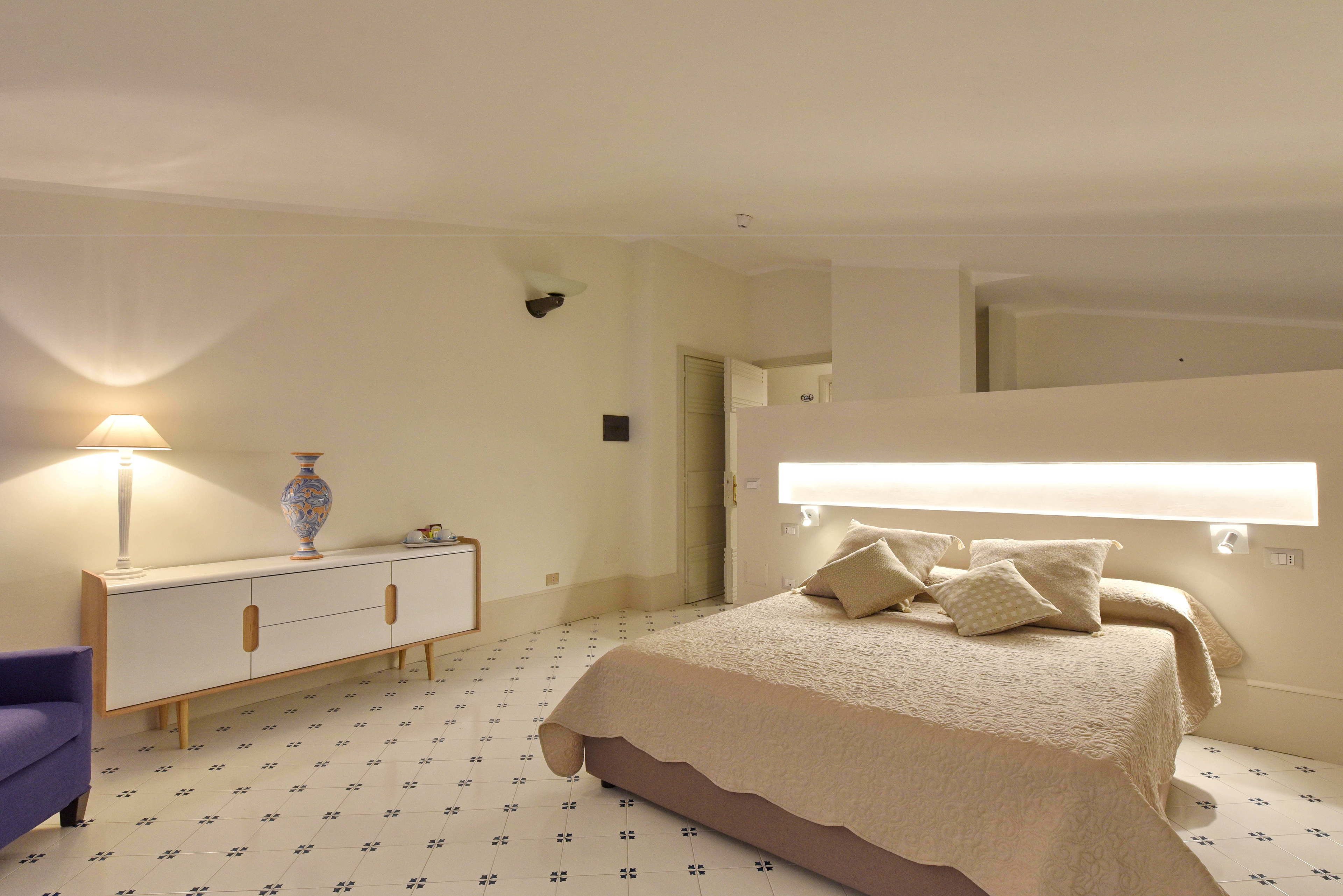Un dormitorio con una cama, una mesita de noche, una lámpara y un aparador.