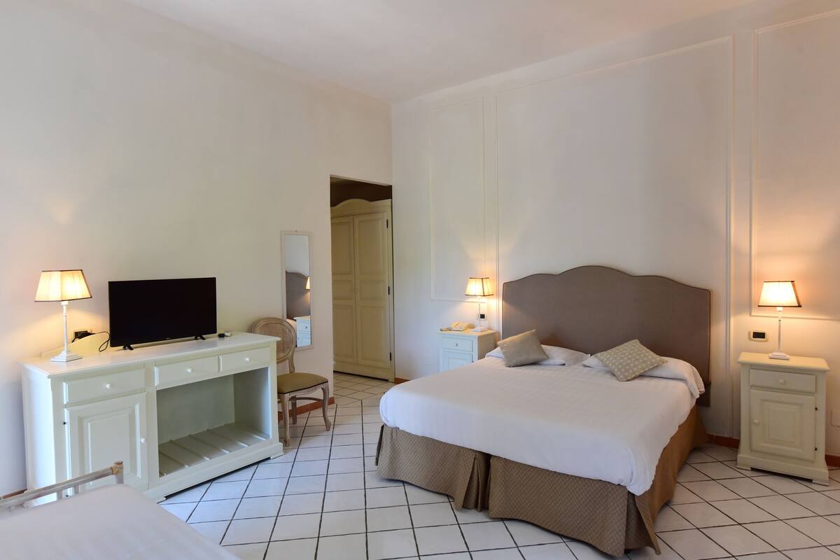 A hotel room with a bed, a TV, a desk, and two bedside lamps.