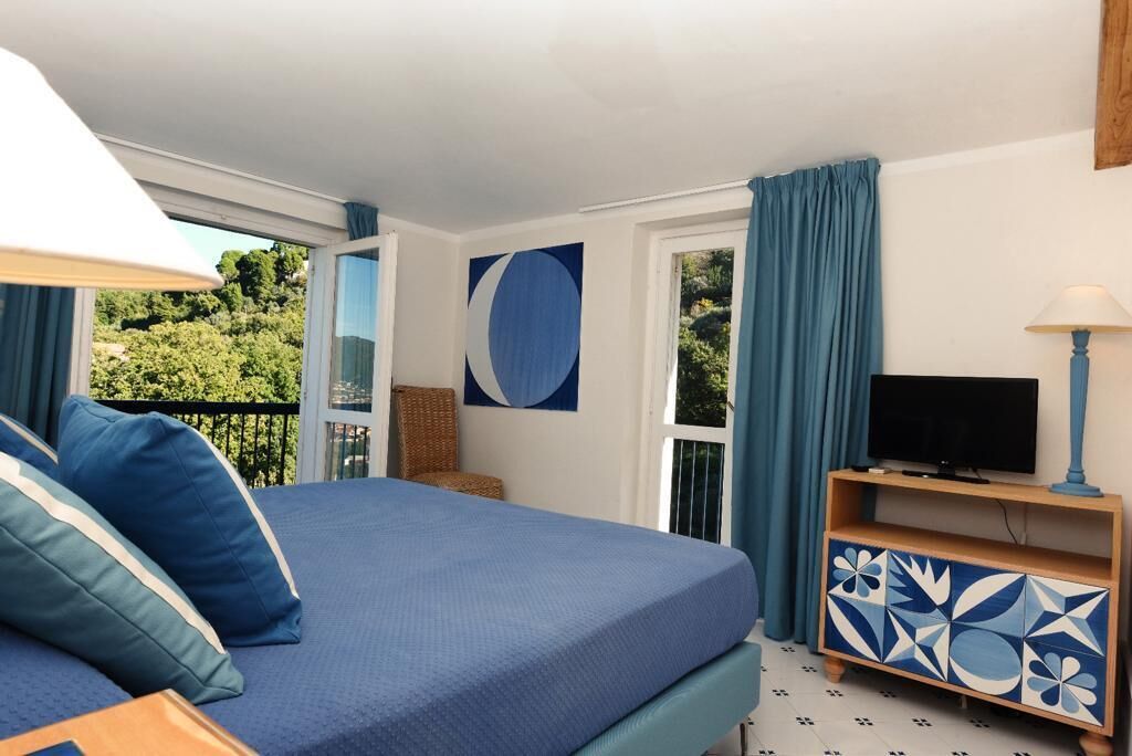 Een slaapkamer met een bed, een televisie op een houten dressoir en uitzicht op groen buiten.