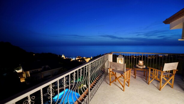 A balcony with a view of the sea, two wooden chairs, a table, and a sign reading "Hotel Garden Riviera".