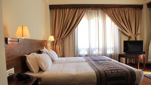 Une chambre d’hôtel avec un lit, un bureau avec un téléphone, un téléviseur posé sur une table d’appoint et des rideaux.
