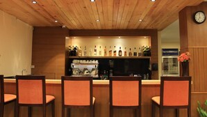 Un espace bar avec un plafond en bois, des tabourets de bar, un réfrigérateur et une horloge au mur.