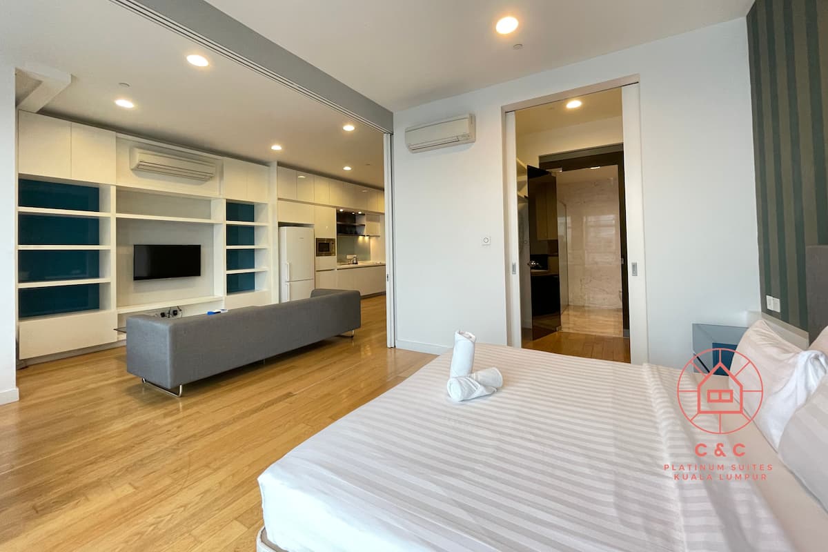 A modern hotel room with a large bed, a sofa, a TV, and a kitchenette.