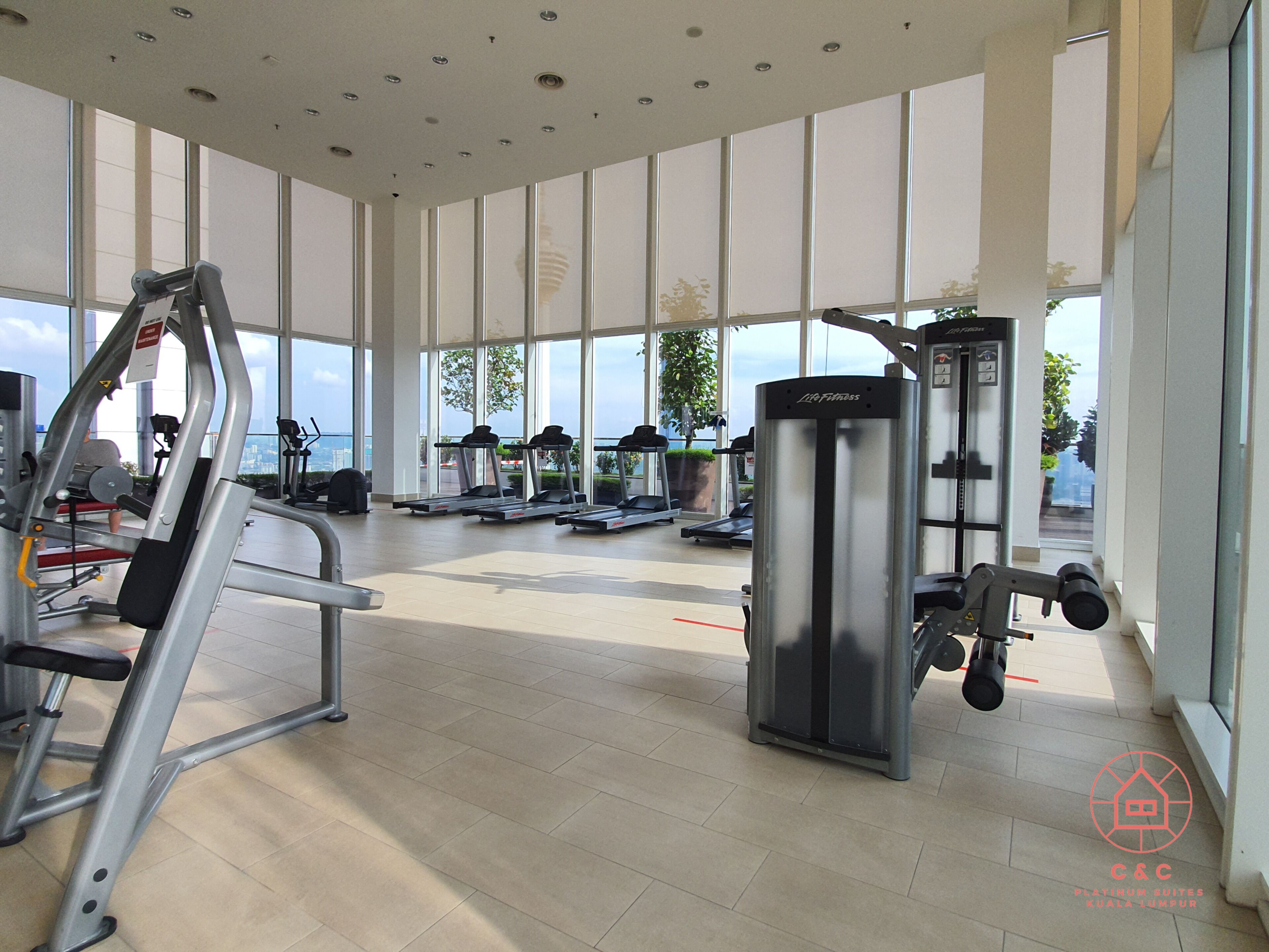 A modern gym with various exercise equipment, large windows, and a view of the city.