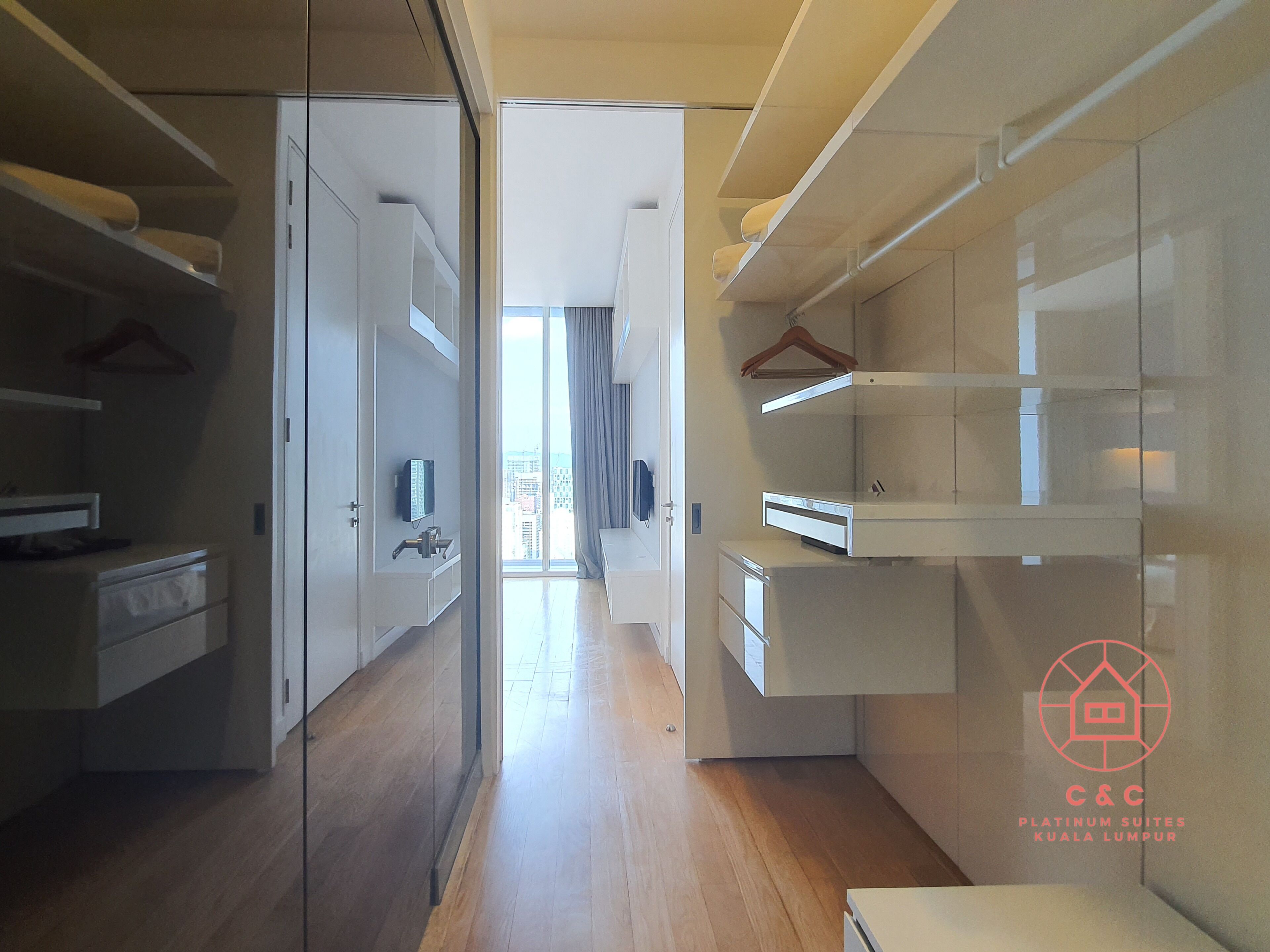 A modern hotel room with a walk-in closet, built-in shelves, and a view of the city.