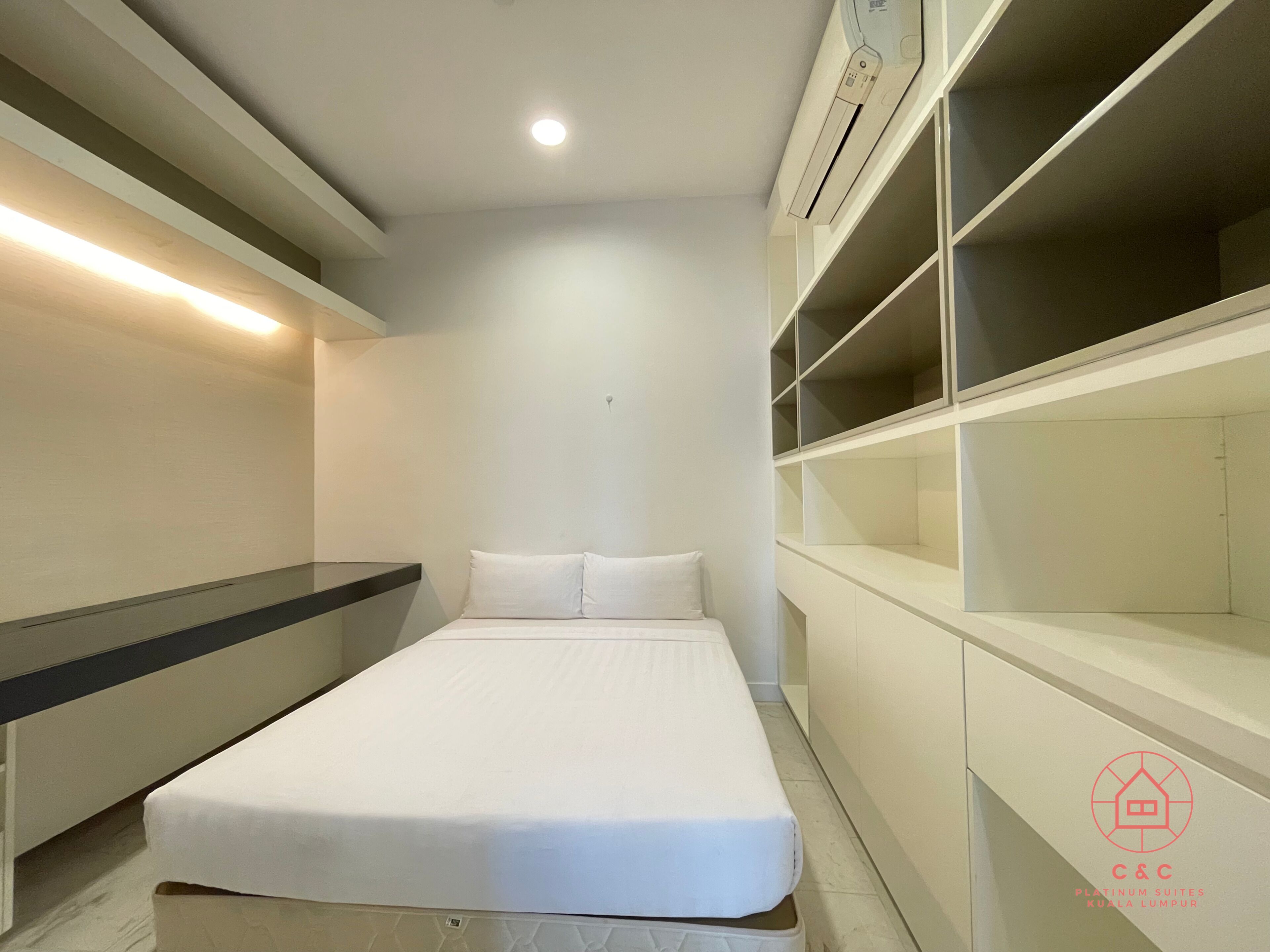 A bedroom with a bed, built-in shelving, and a ceiling light.