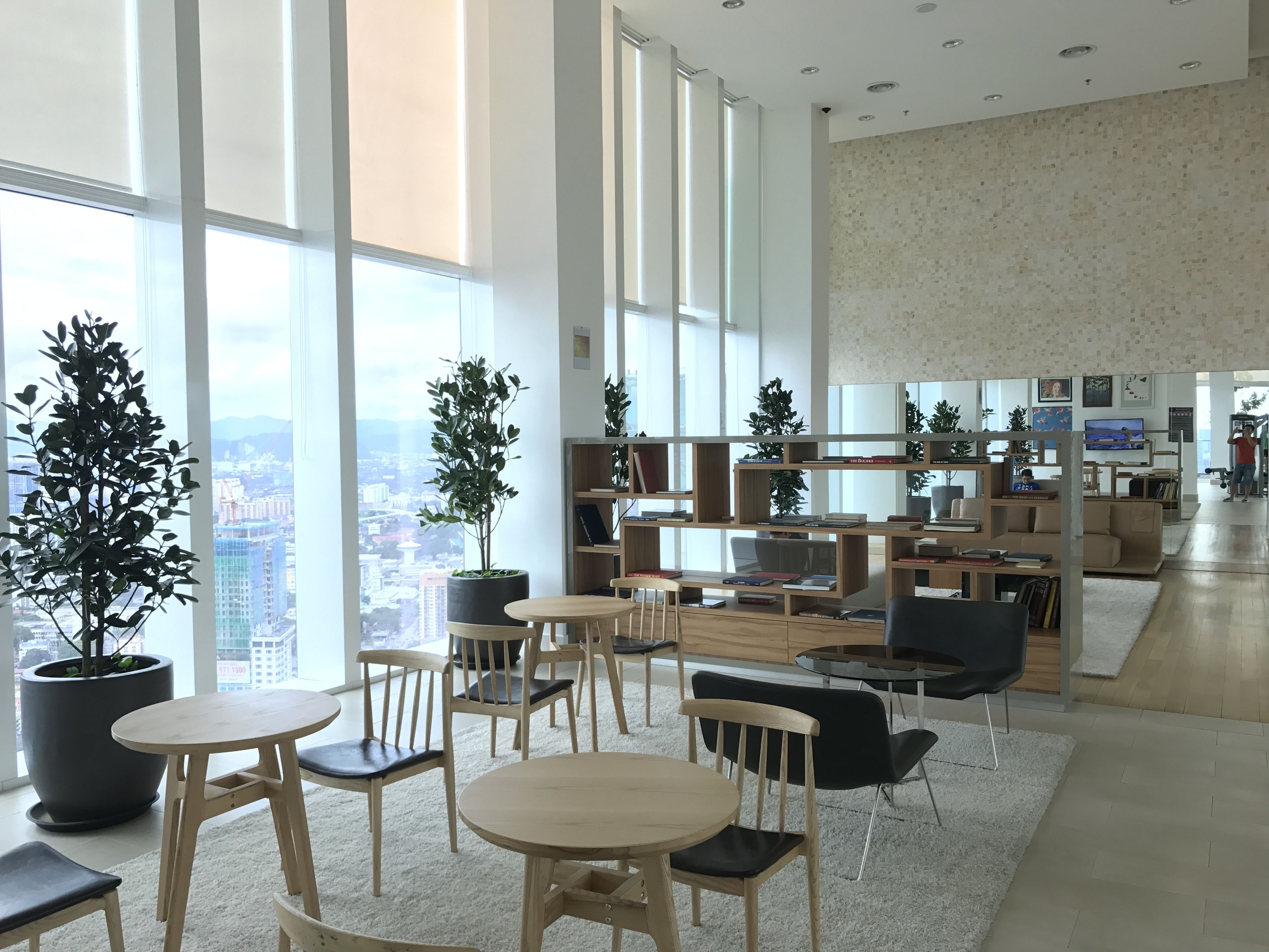 A spacious, well-lit indoor area with large windows, multiple seating arrangements, and a variety of bookshelves.