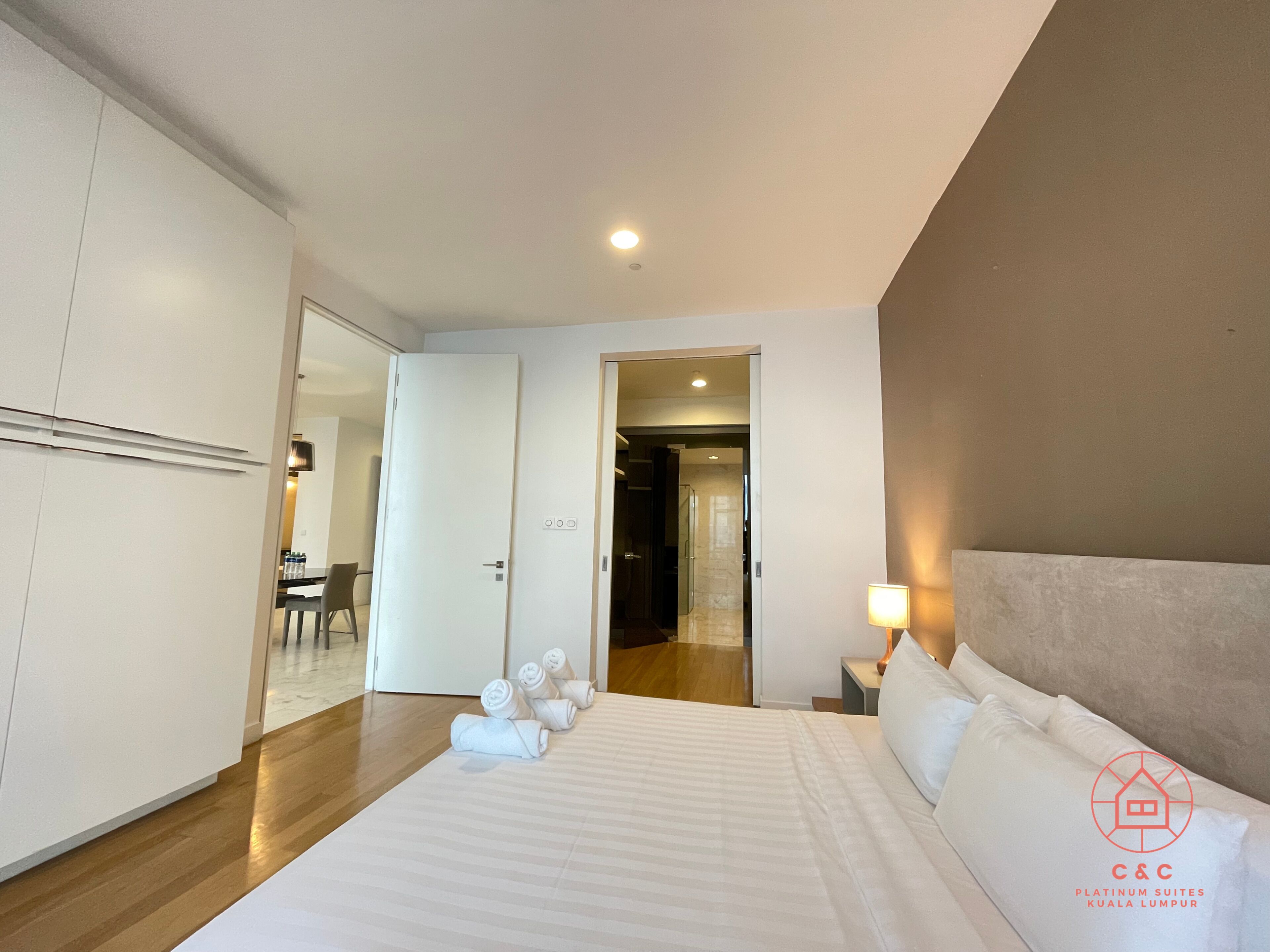 Une chambre d’hôtel avec un lit, un bureau et une chaise. Il y a des serviettes sur le lit et une lampe sur la table de chevet.