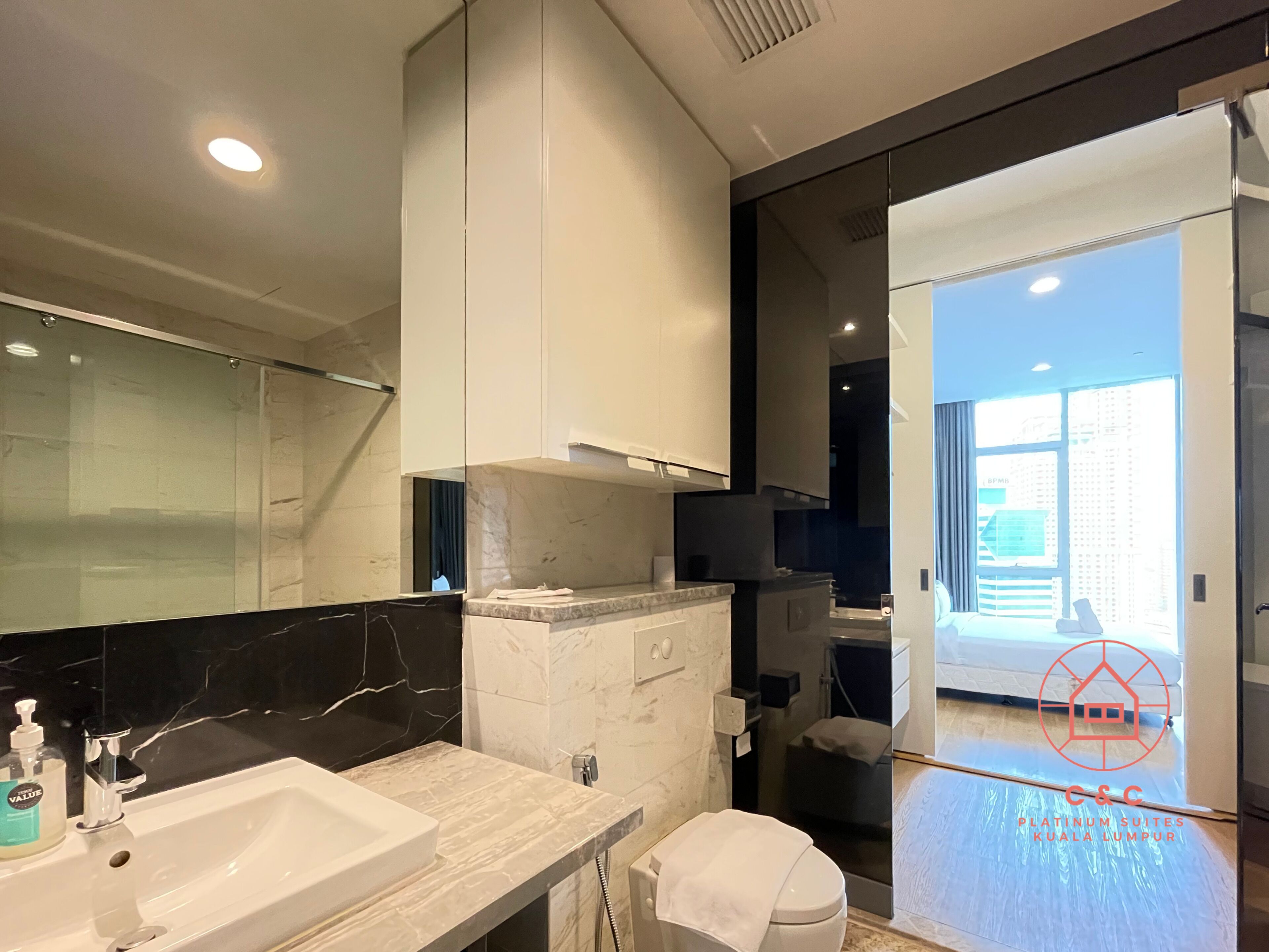 A modern bathroom with a large mirror, a sink, and a shower. There is a view of a cityscape through the window.