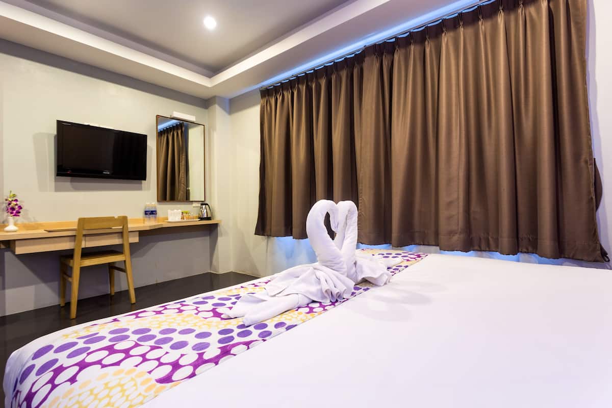 A hotel room with a bed, a desk, a chair, a TV, and a window with curtains.