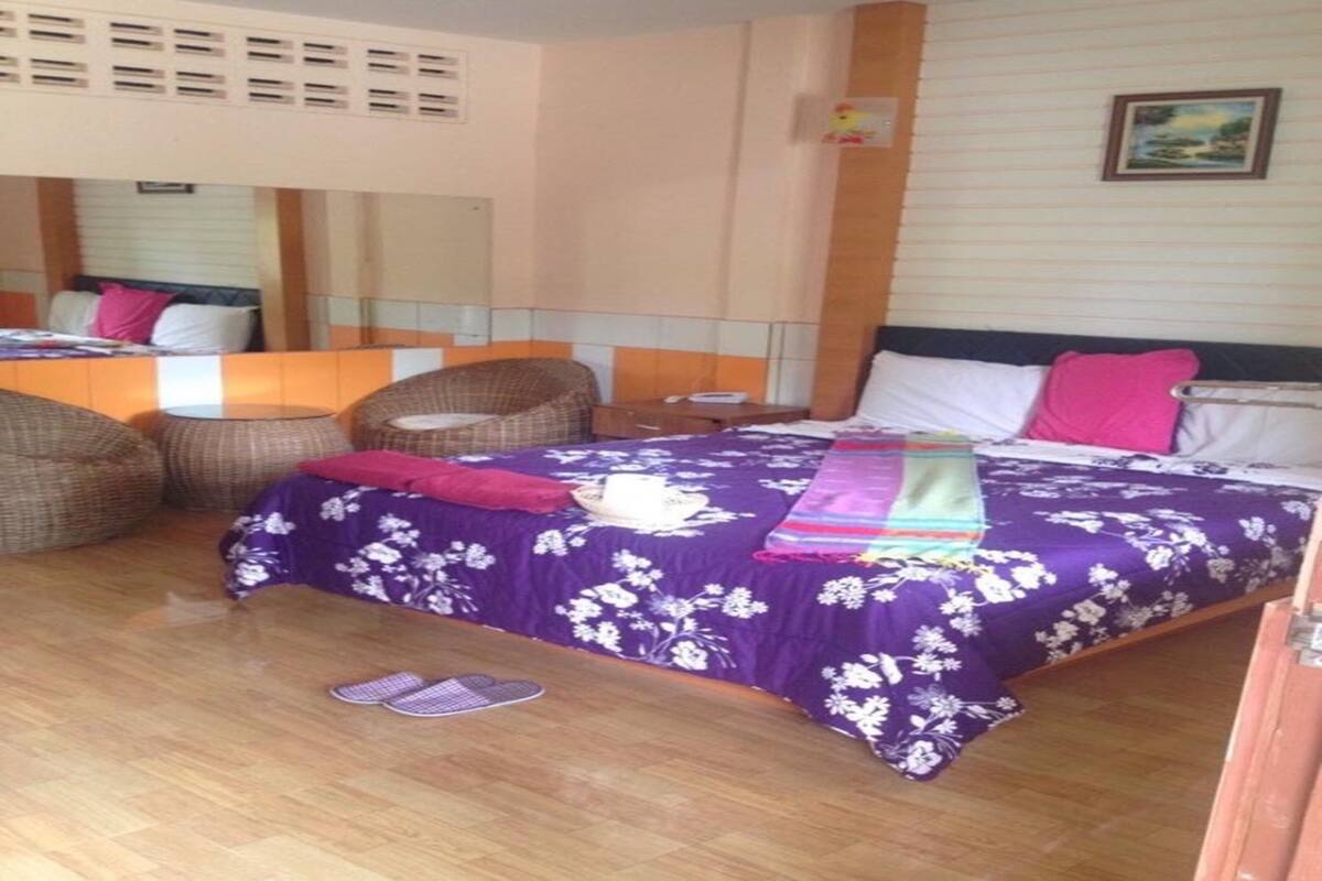 A bedroom with a bed, two wicker chairs, a nightstand, and a mirror.
