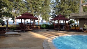 Zona de piscina con gazebos de madera y sillones de descanso, rodeada de árboles y vistas al mar.