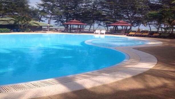 Una piscina de borde curvo, rodeada de sillas de descanso y zonas con sombra.