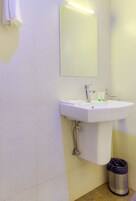 Un baño con un lavamanos blanco, espejo y cubo de basura.