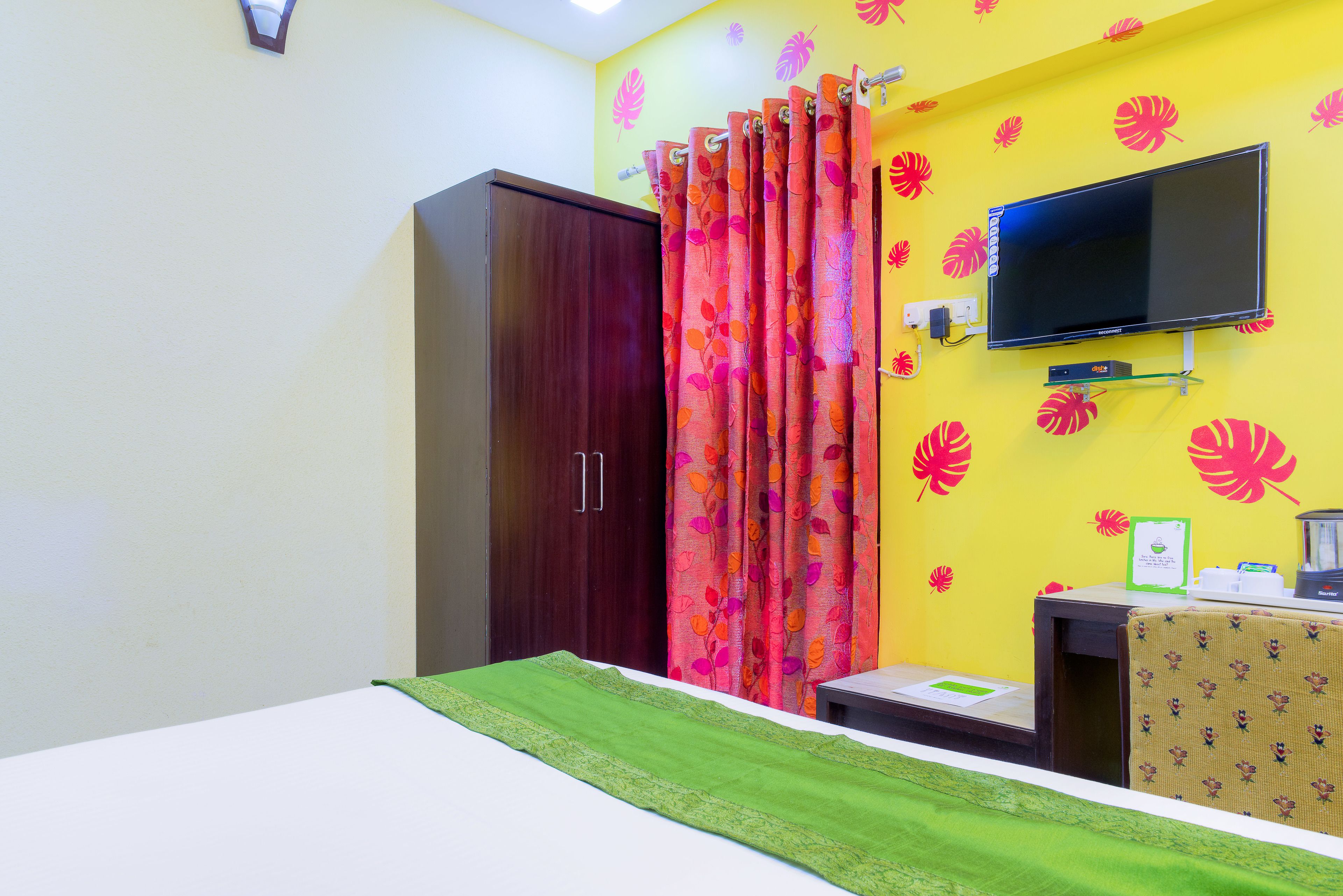 A room with a bed, a wardrobe, a TV mounted on the wall, and a desk with a chair.