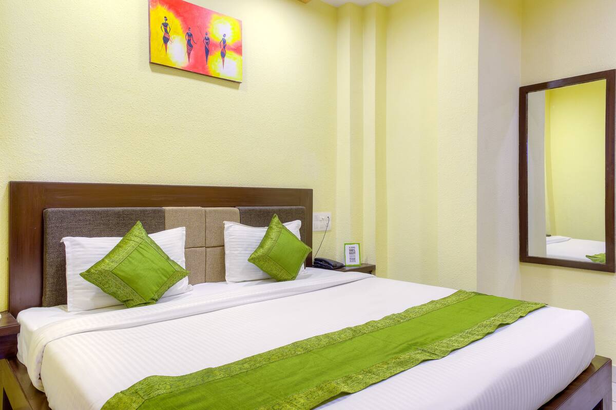 Una cama bien tendida con sábanas blancas y detalles verdes, un cabecero de madera y un cuadro sobre ella.
