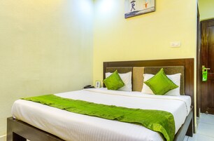 Un letto rifatto con cuscini e copripiumone verdi, una testiera in legno, una sveglia a muro e una porta con un cartello verde.