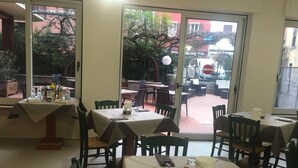 Un comedor interior con mesas y sillas, vistas al exterior a través de puertas de vidrio, y una pequeña mesa con salsas y un menú.