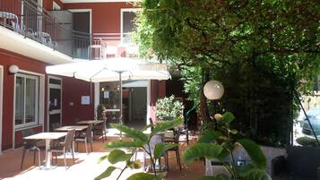 An outdoor patio area with tables and chairs, umbrellas, and a tree providing shade.
