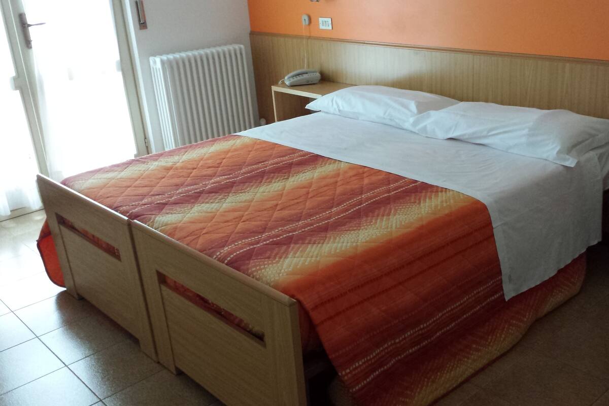 A hotel room with a bed, a bedside table, a chair, and a radiator.