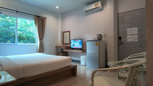 A hotel room with a bed, a television, a refrigerator, a window with curtains, and a door. - Seree Grand Resort (Hat Yai)