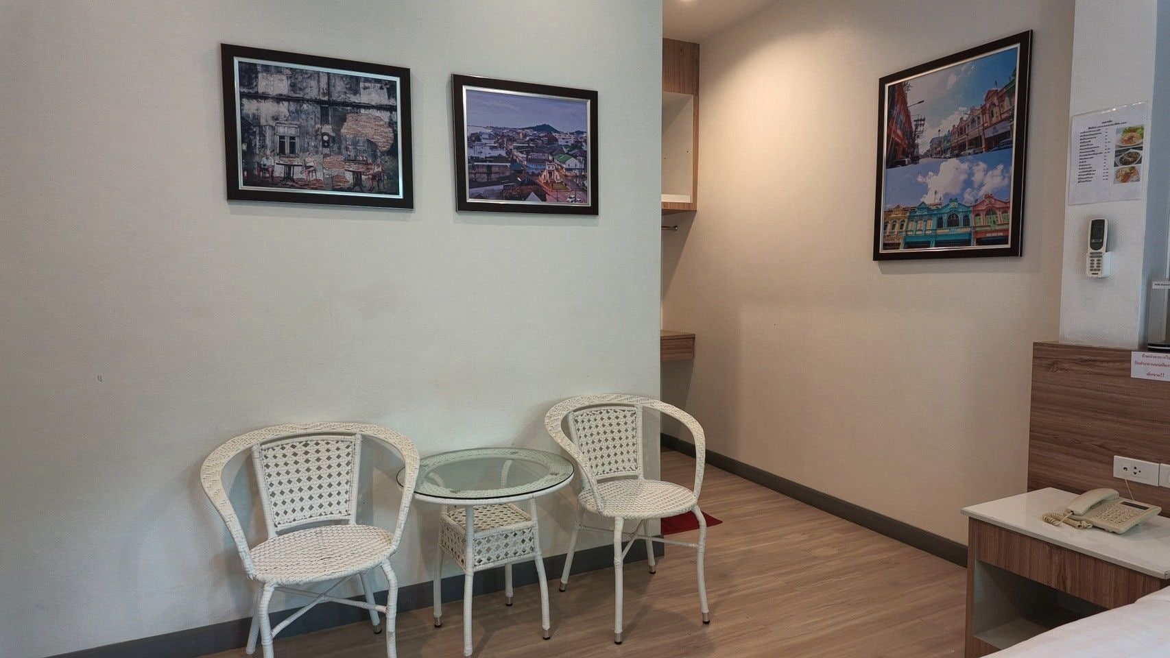 A hotel room with a small table and two chairs, a bed, a wooden desk with a telephone, and three framed pictures on the wall.