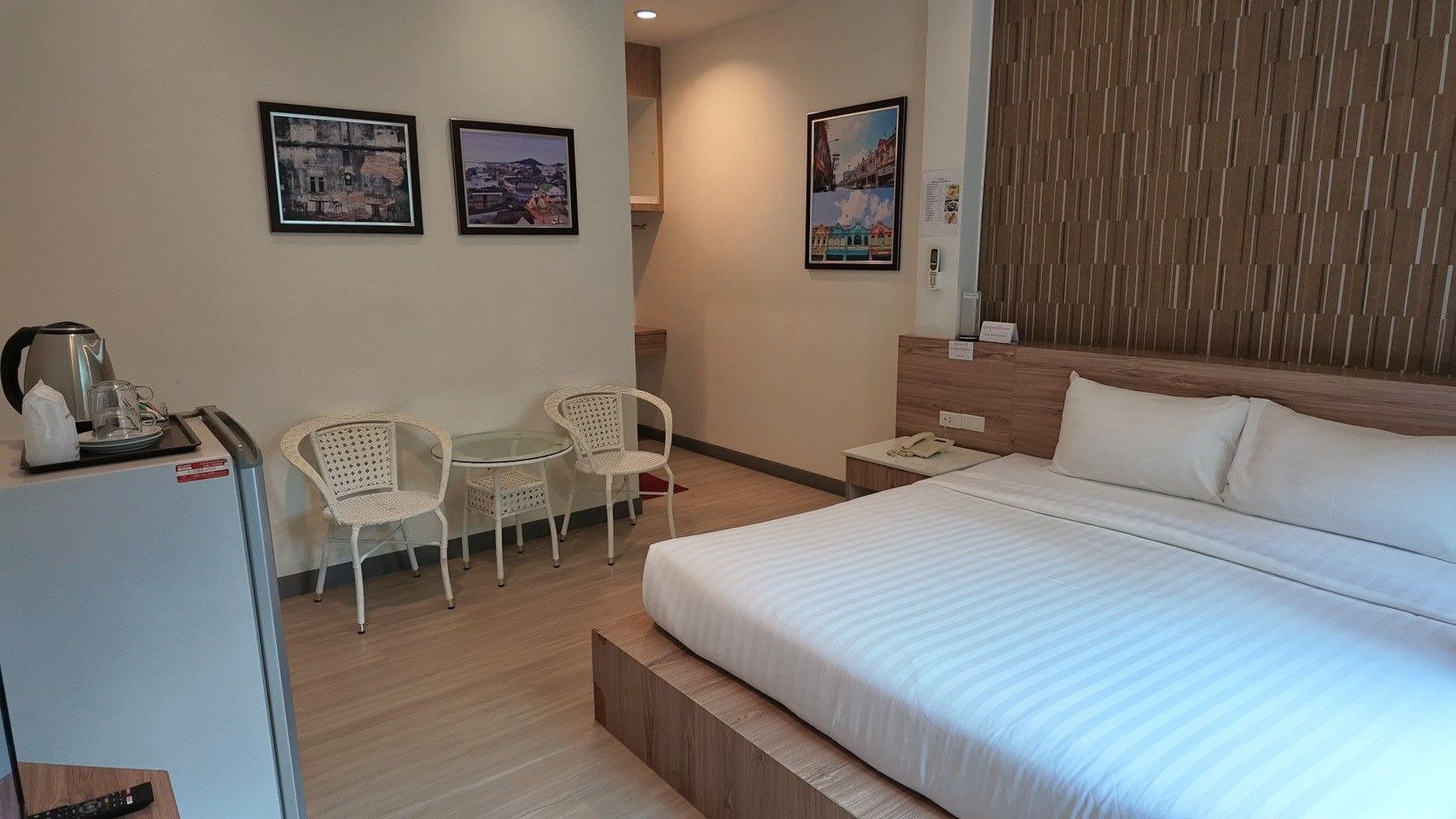 A hotel room with a bed, a small table with chairs, a refrigerator, and wall art.