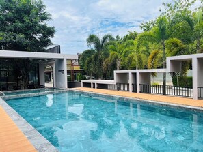 A swimming pool with a wooden deck, surrounded by modern architecture and tropical plants. - Seree Grand Resort (Hat Yai)