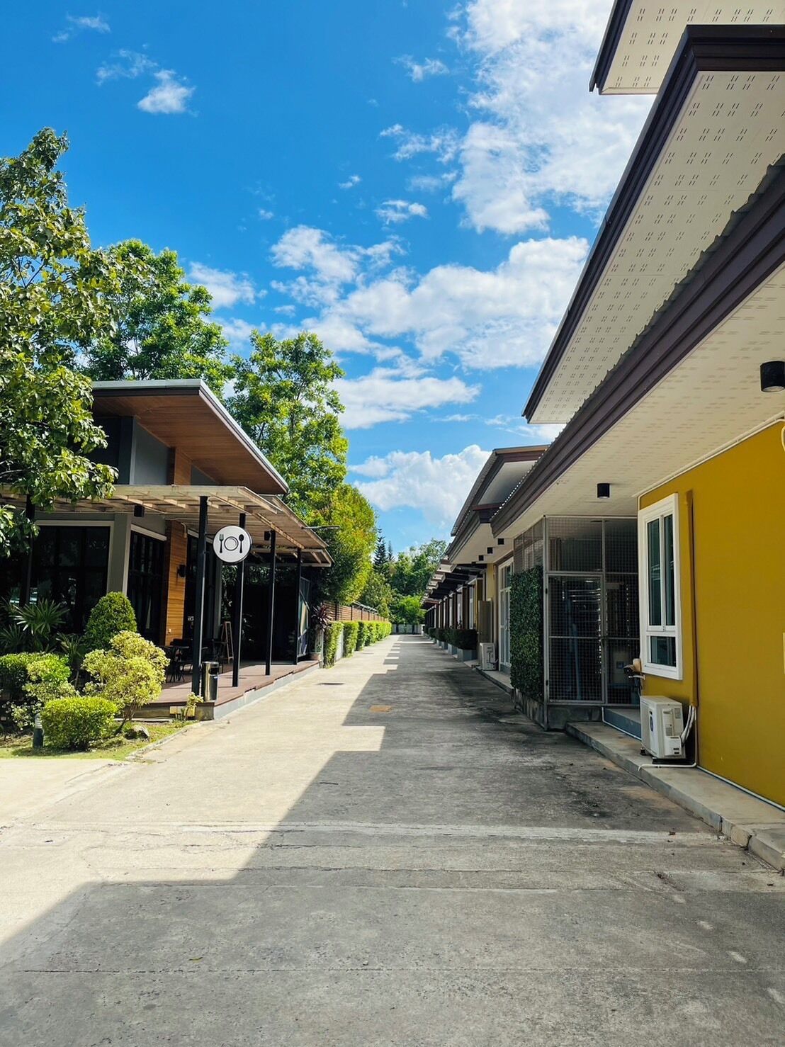A street lined with buildings, including a restaurant with outdoor seating and a yellow building with a large window.