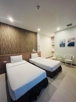 A hotel room with two single beds, a wooden headboard, a small table with chairs, and artwork on the wall. - Seree Grand Resort (Hat Yai)