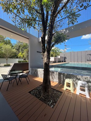 A modern outdoor area with a wooden deck, a pool, and a tree. - Seree Grand Resort (Hat Yai)