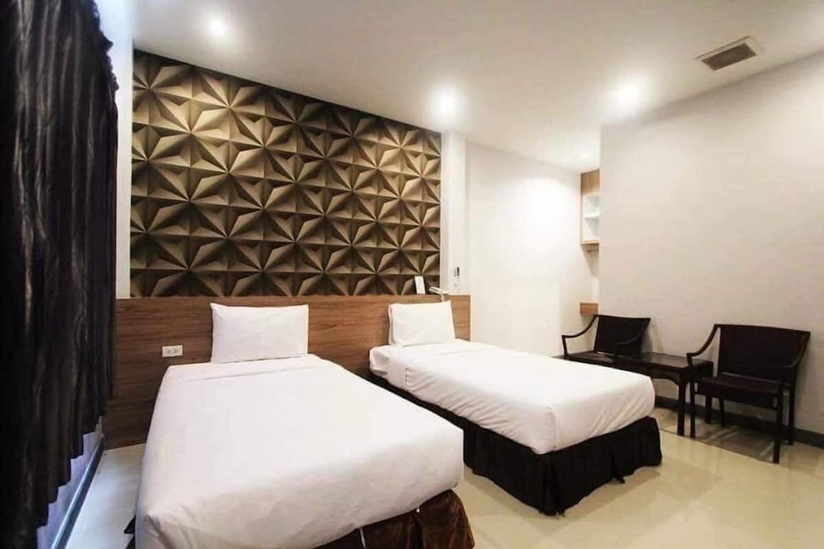 A hotel room with two single beds, a wooden headboard, a geometric wall panel, a desk, and a chair.