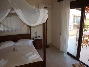 A bedroom with a canopy bed, a bedside table with a lamp, and a view of the outdoor patio area. - Villa Helidoni (Platanias)