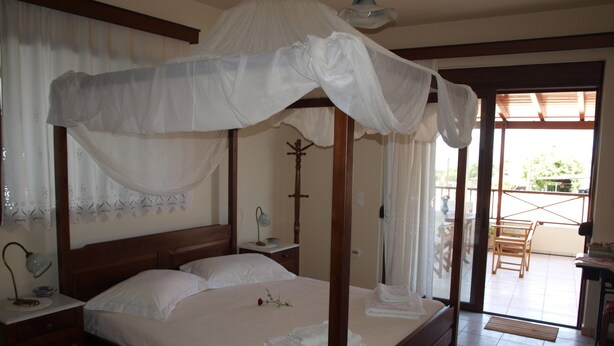 Una cama con dosel y blancas sábanas, una mesita de noche con lámpara, y vista del patio exterior a través de una puerta de cristal.