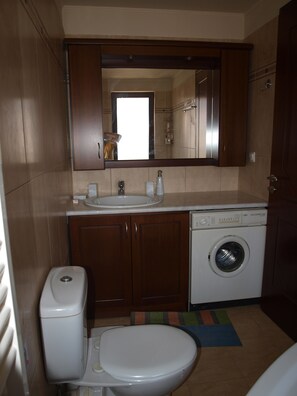 A compact bathroom with a toilet, sink, and washing machine. - Villa Helidoni (Platanias)