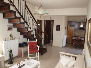 Amplia sala de estar con una escalera, una mesa de comedor y una cocina al fondo.